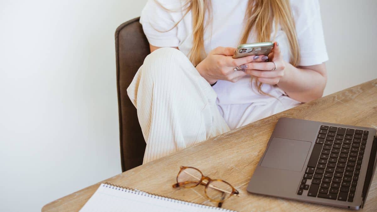 How to find freelance work in the UK - image shows a woman using her phone in front of a laptop